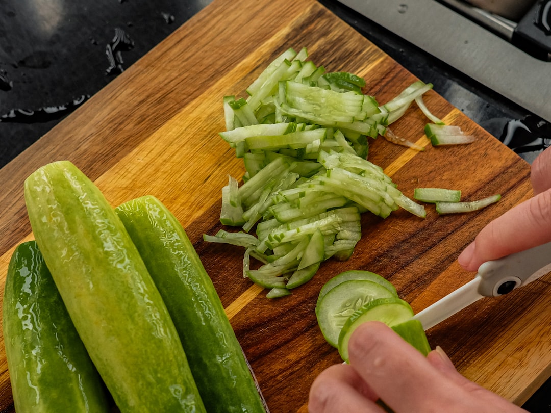 Chopping fresh cucumbers on a wooden cutting board.